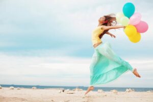 Happy girl holding bunch of colorful air balloons at the beach